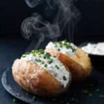 Zwei aufgeschnittene Ofenkartoffeln mit Hüttenkäse-Dip und Schnittlauch